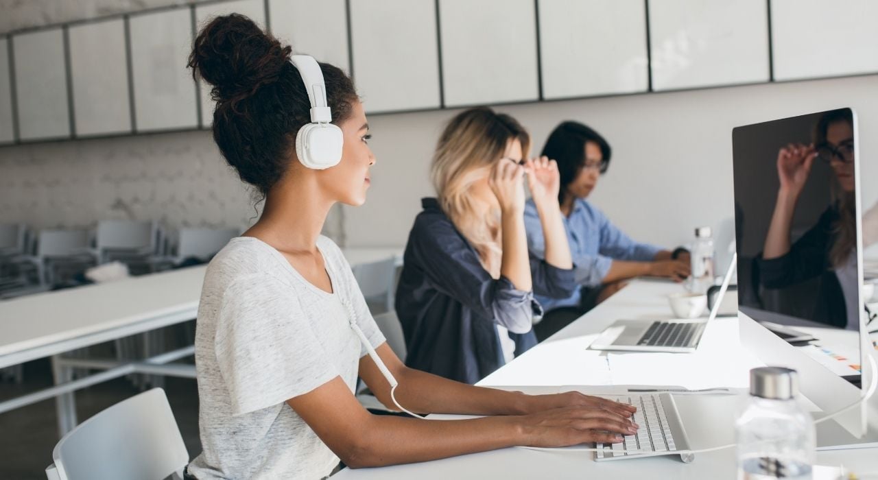 vrouw met headphones aan het werk op een laptop met 2 collega's naast haar