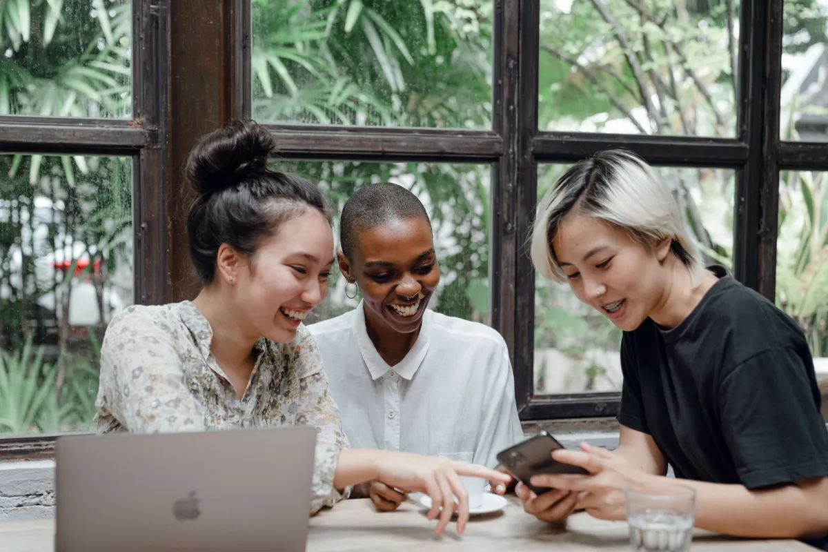 Trois femmes qui rigolent en regardant un smartphone avec un macbook
